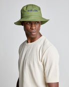 A man wearing a green bucket hat with the brand 'FIELDS' embroidered on it, paired with a beige knit sweater.