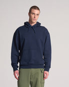 A person wearing a navy blue hooded sweatshirt with a kangaroo pocket and drawstrings, paired with green pants.