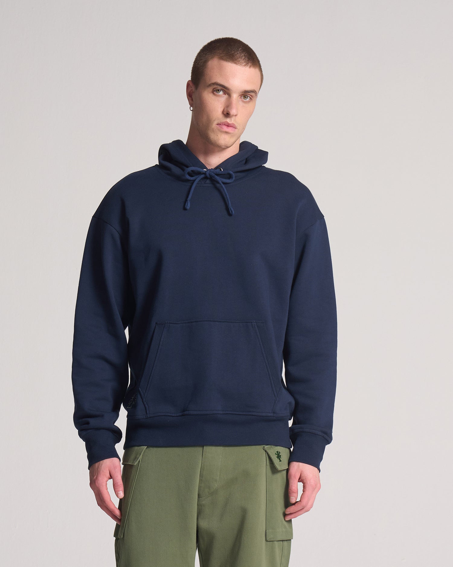 A person wearing a navy blue hooded sweatshirt with a kangaroo pocket and drawstrings, paired with green pants.