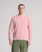 A person wearing a round neck, pink sweater made from cotton.