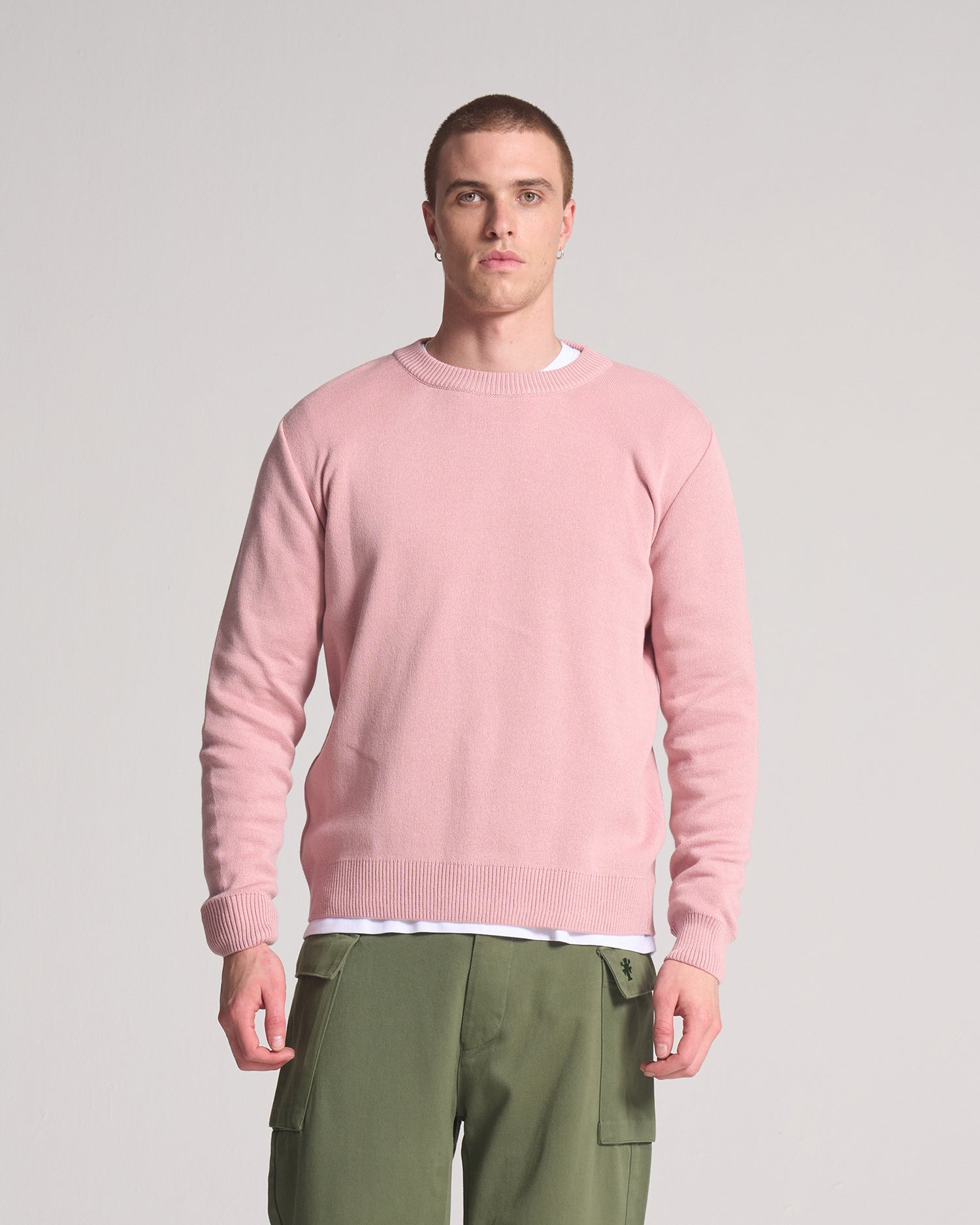 A person wearing a round neck, pink sweater made from cotton.