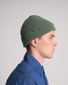 Person wearing an olive green knit beanie against a plain background
