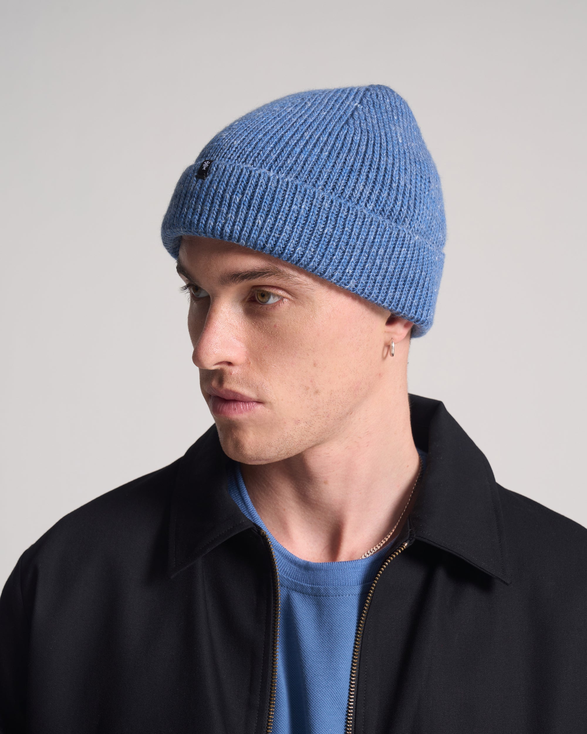 Man wearing a blue knit beanie and black jacket on a gray background