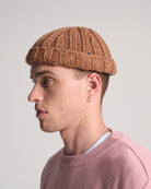 Person wearing a brown knitted beanie and pink sweater against a plain background