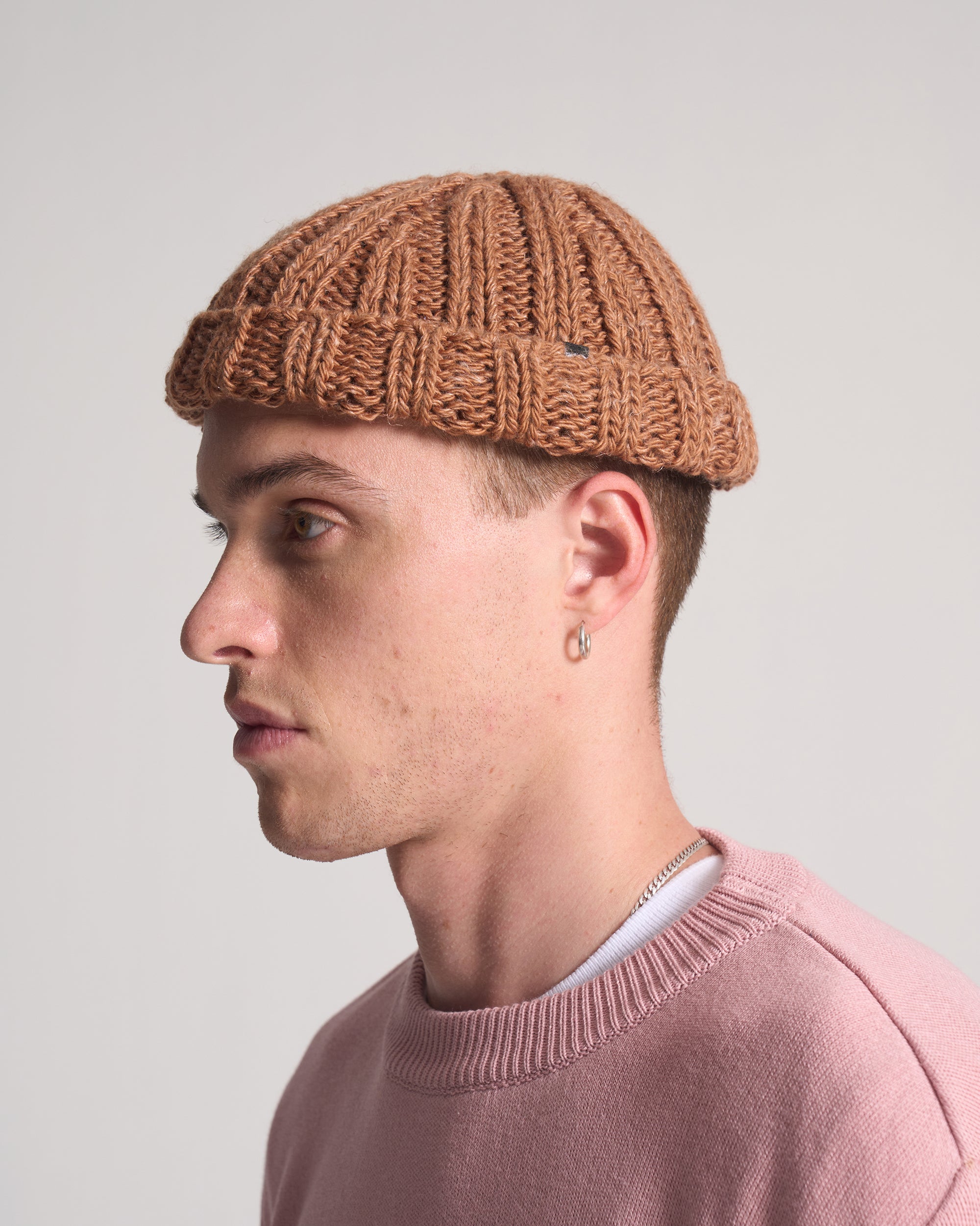 Person wearing a brown knitted beanie and pink sweater against a plain background
