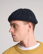 Man wearing a black knit beanie and mustard yellow sweater against a plain background