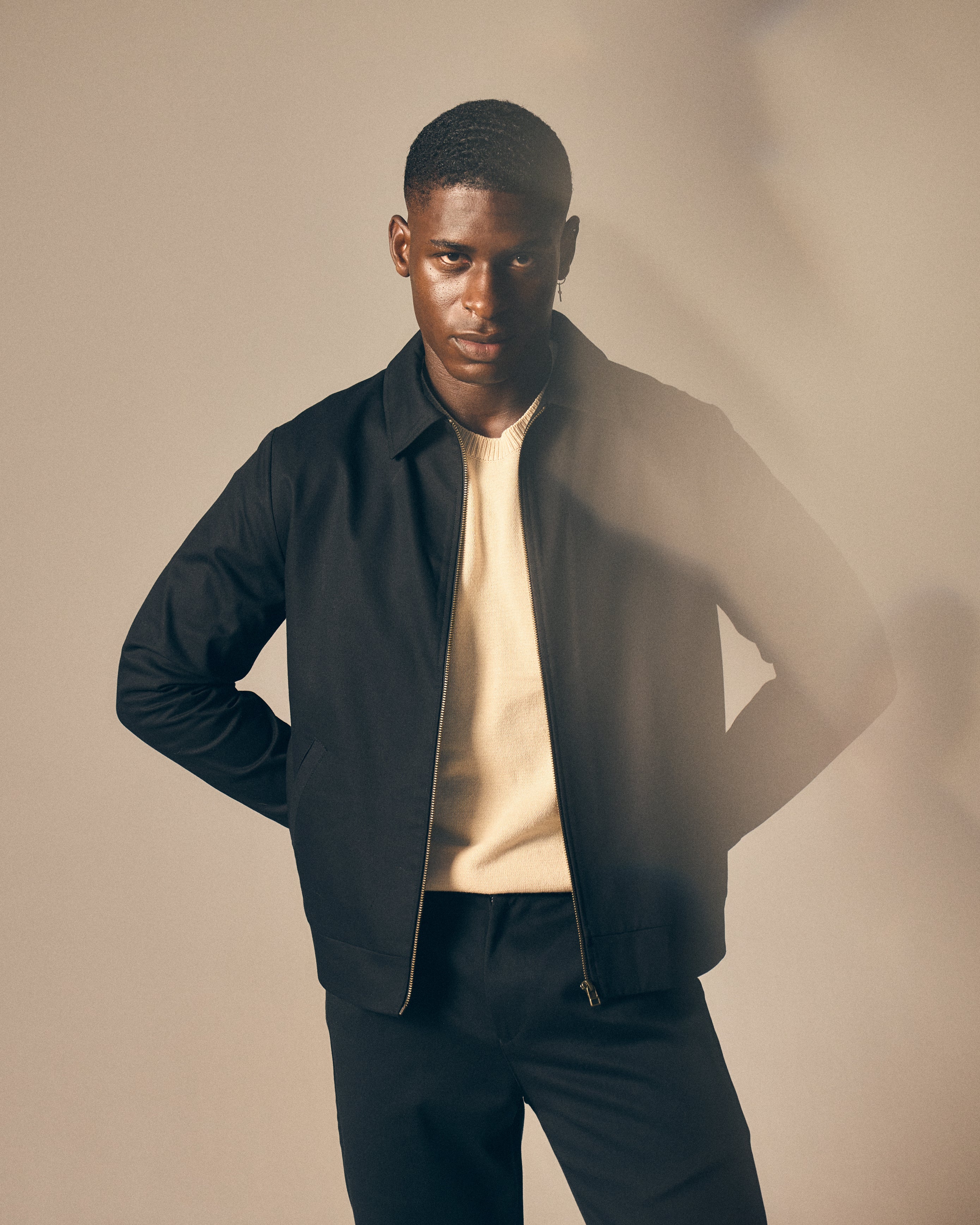 Man wearing a black jacket over a beige shirt with a plain background
