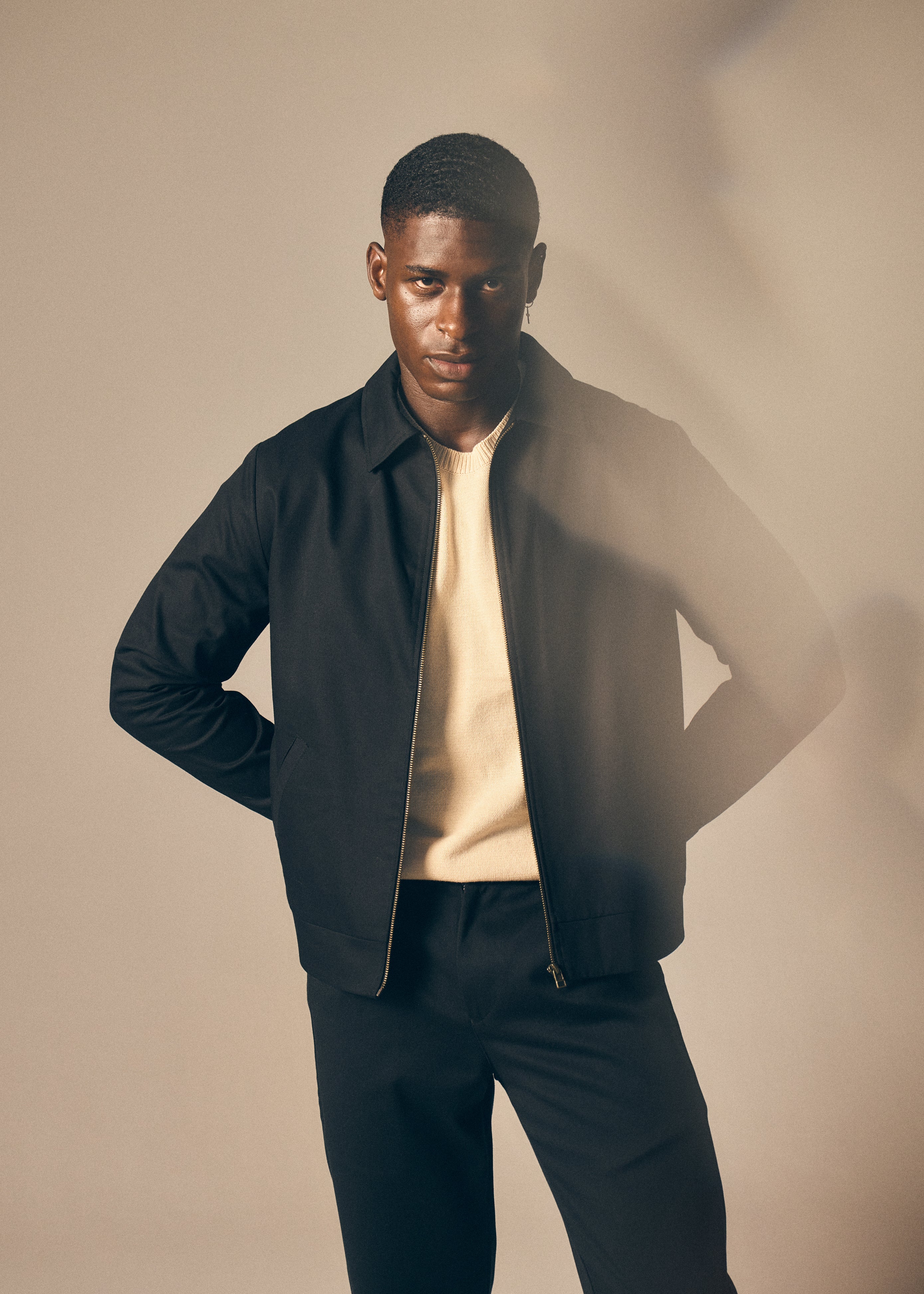 Man wearing a black jacket over a beige shirt with a plain background