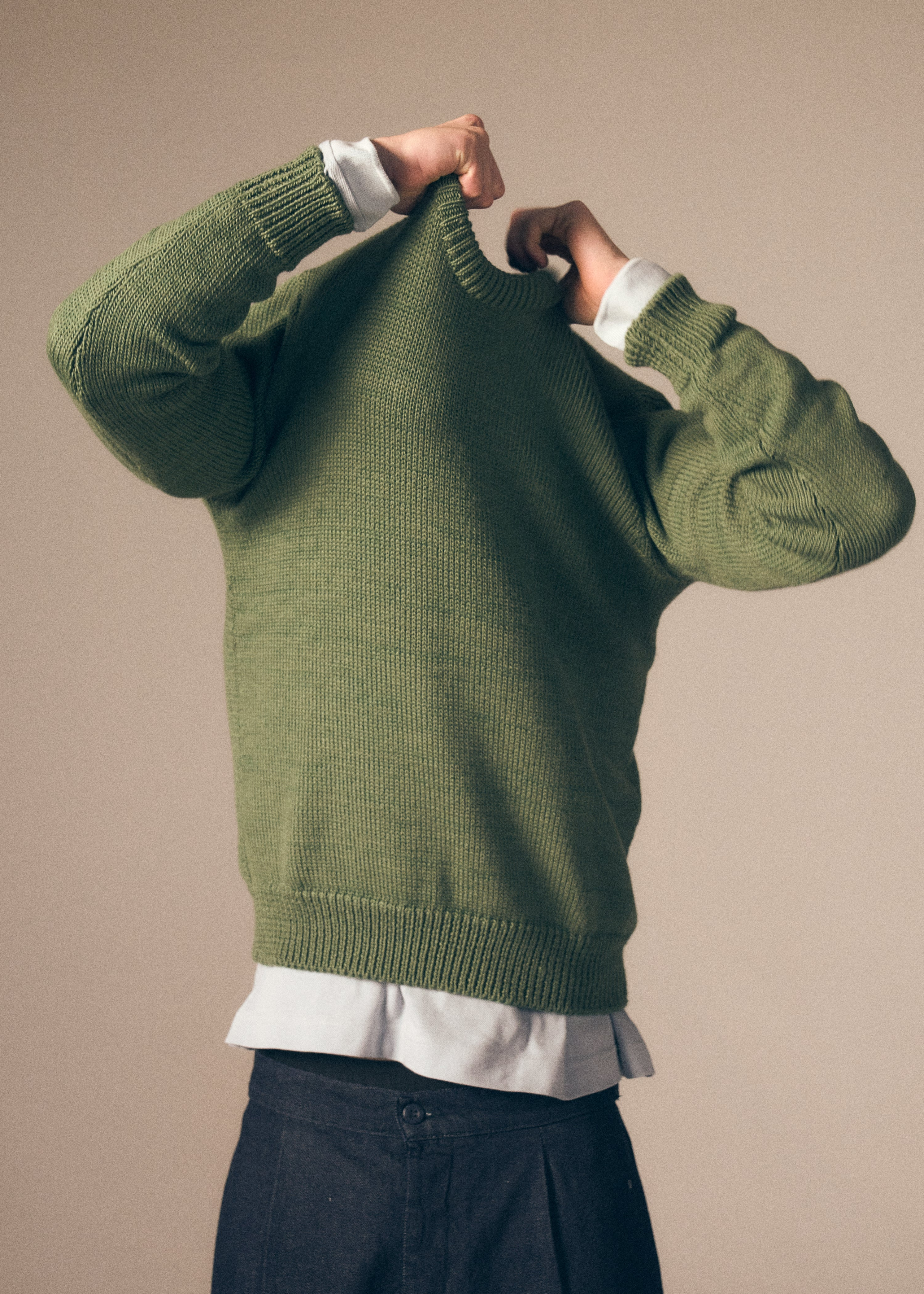 Person wearing a green sweater over a white shirt with a beige background with denim 12.5 oz trousers