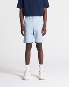 A person standing wearing light blue cotton twill art shorts with a fitted silhouette, including front quarter-slant pockets, a single coin pocket, back welt pockets, and a zip fly.