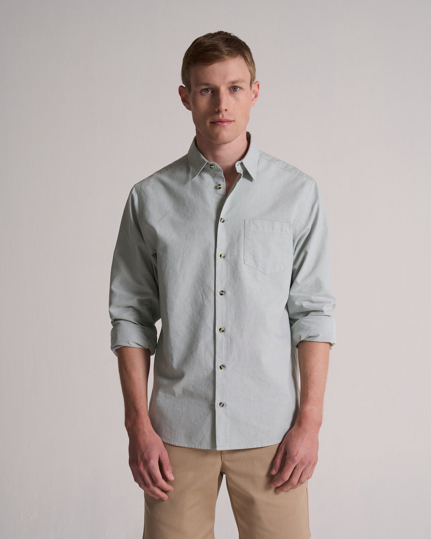 Man wearing a light green button-up shirt with rolled-up sleeves against a plain background