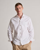 Man wearing a white dress shirt with a plain background.