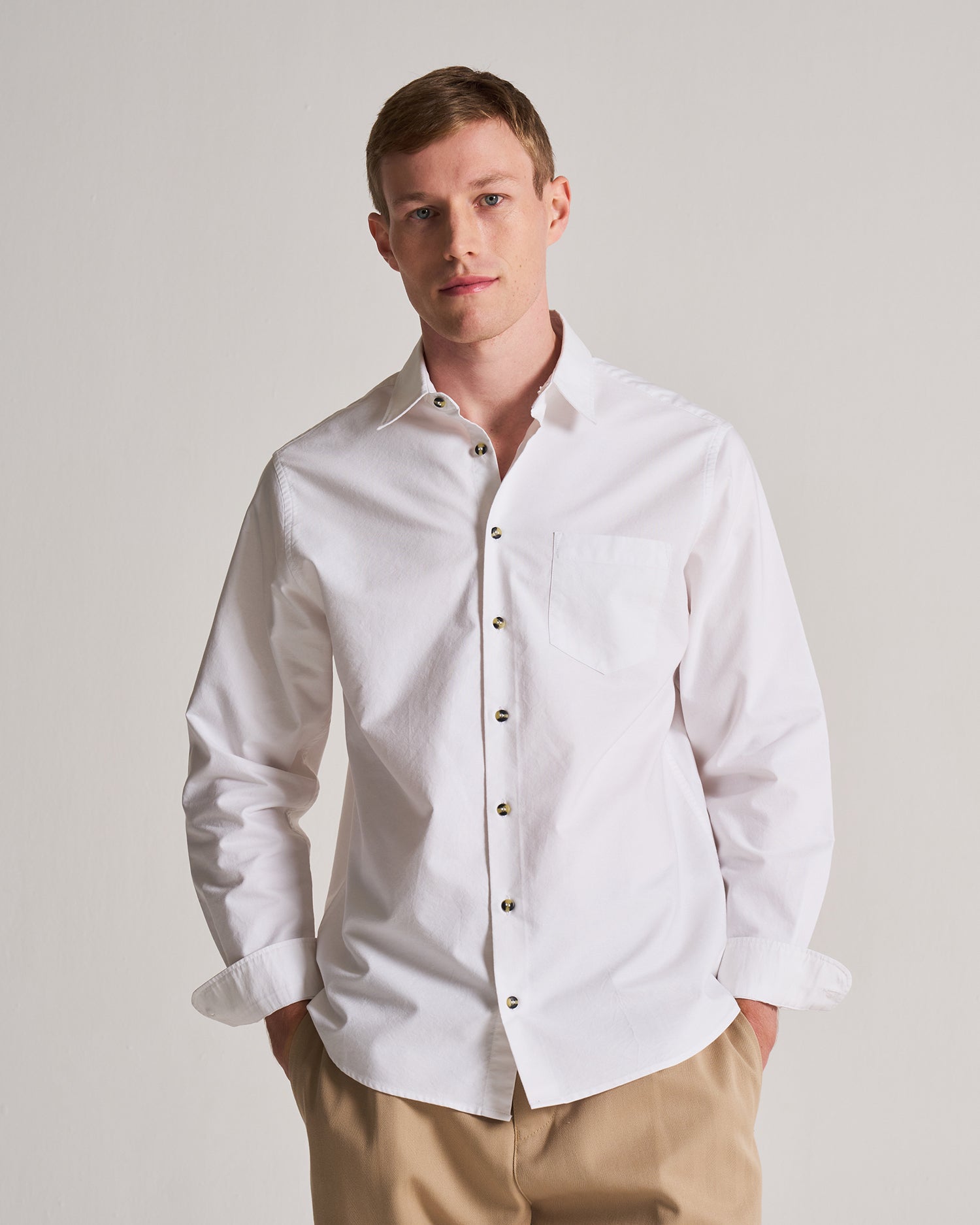 Man wearing a white dress shirt with a plain background.