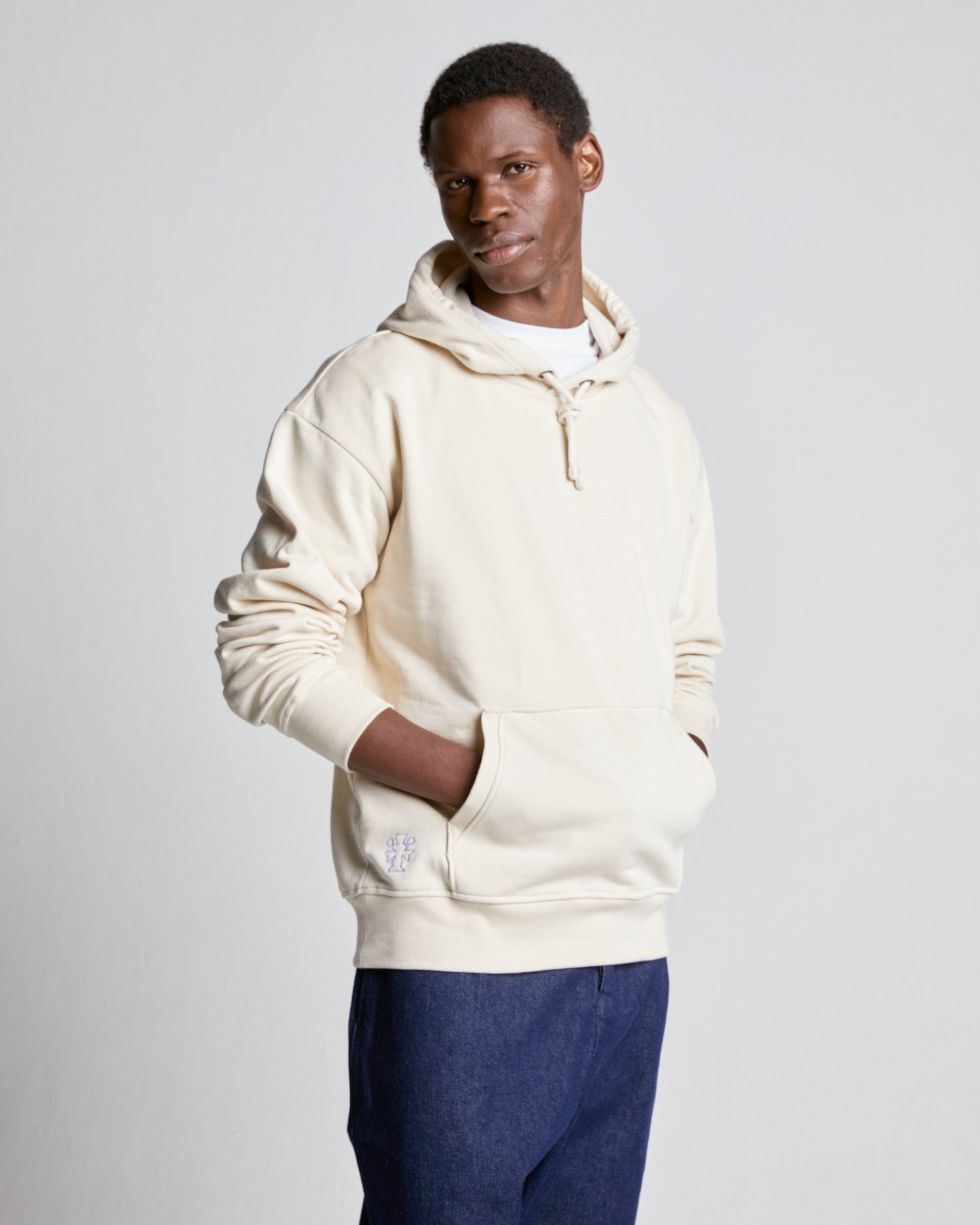 A person wearing a ecru hooded sweatshirt with the FIELDS brand logo visible on the lower left side of the hoodie.
