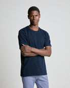 A person wearing a navy knitted tee and light trousers, standing with arms crossed.
