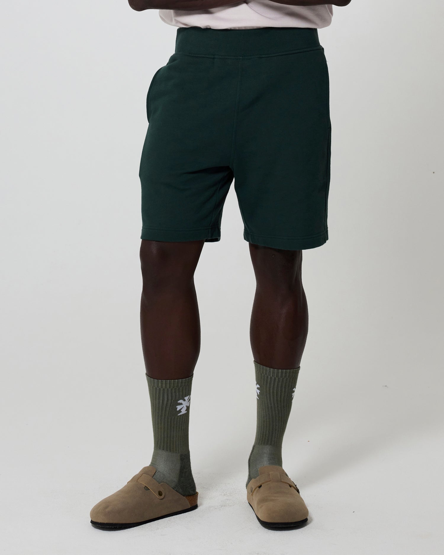 Person wearing dark green lounge shorts, olive socks, and tan shoes on a white background. Clothing from Fields.