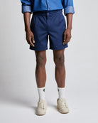 A person standing wearing relaxed fit navy cotton shorts, a blue shirt, white socks, and beige shoes.