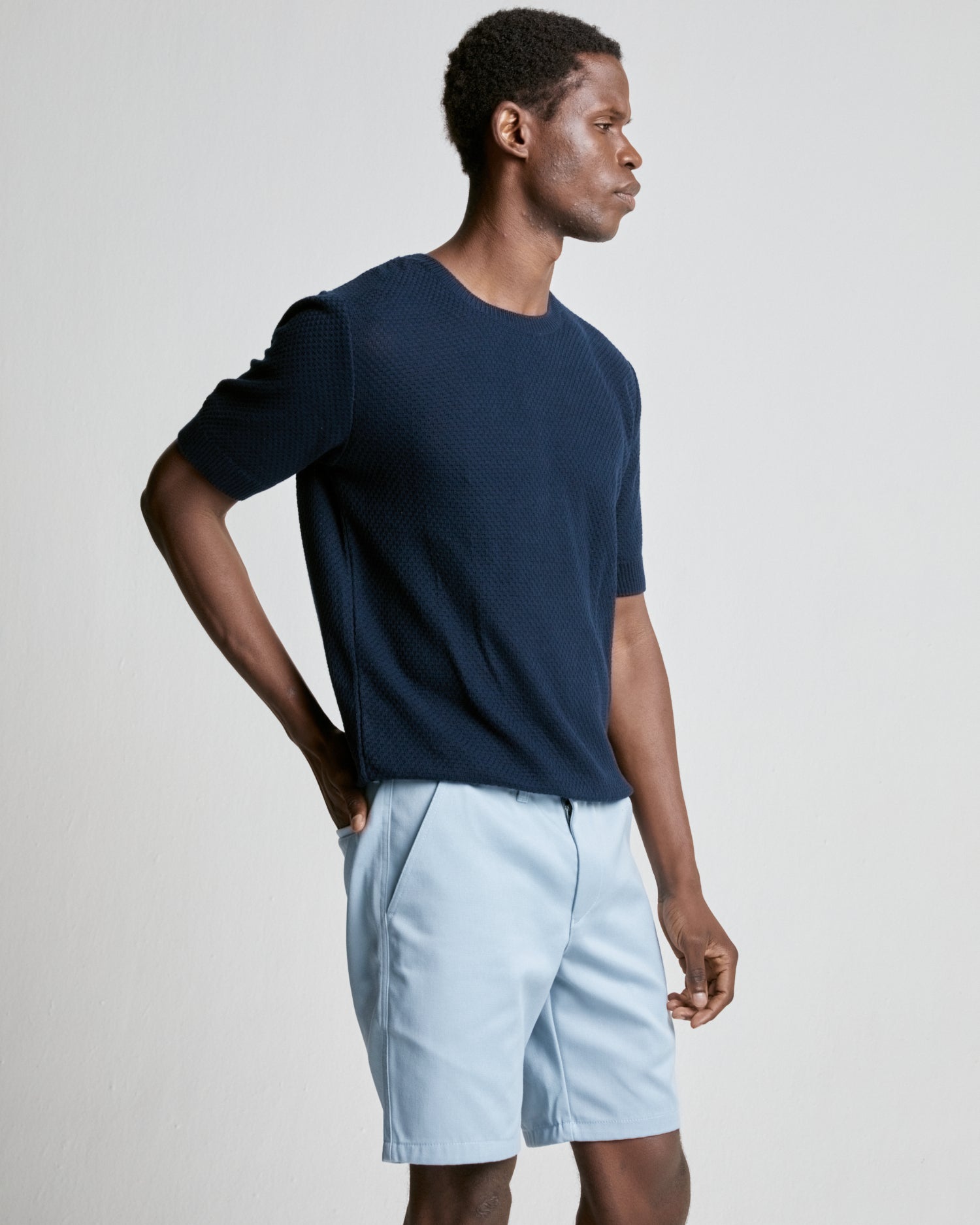 A man wearing a navy blue waffle knitted tee with short sleeves and light blue shorts.