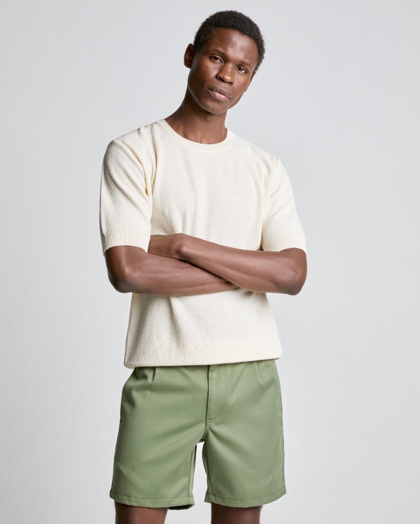 A male model wearing an ecru color waffle knitted tee with short sleeves and green shorts.