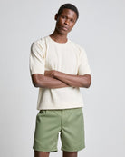 A male model wearing an ecru color waffle knitted tee with short sleeves and green shorts.