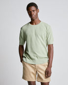 A man wearing a green waffle knitted tee with short sleeves and beige shorts.