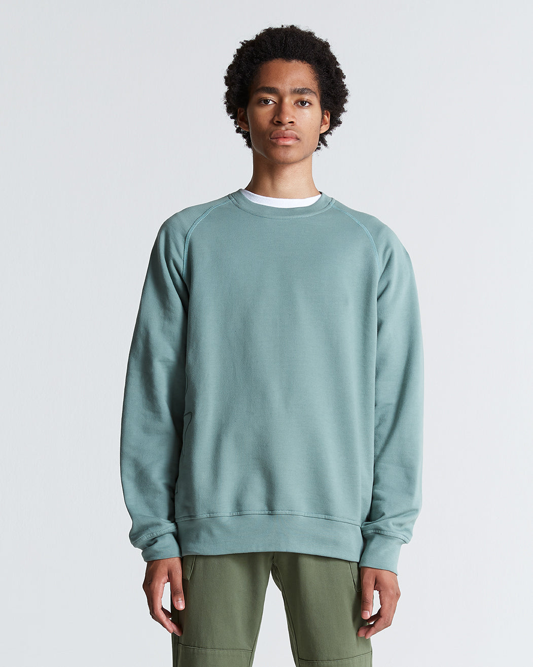 A person wearing a green, sea-spray, crew neck, long-sleeved simple sweater.