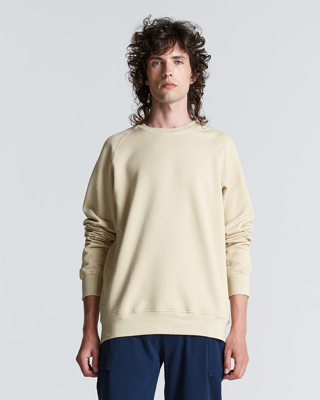 A person wearing a beige simple sweater with a crew neck, made from cotton, and paired with dark pants.