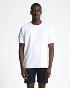 A person wearing an oversized cotton white crew neck t-shirt, the box tee by FIELDS and black shorts.
