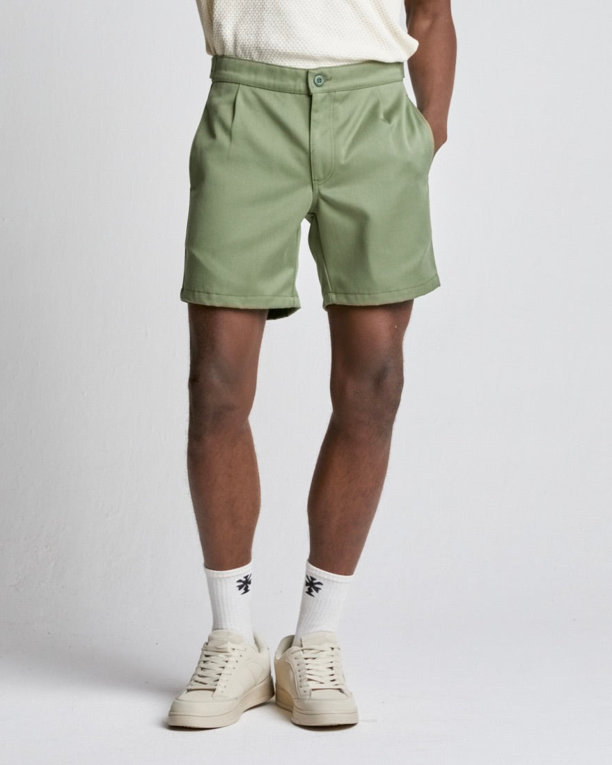A person wearing relaxed fit green cotton shorts and white sneakers.