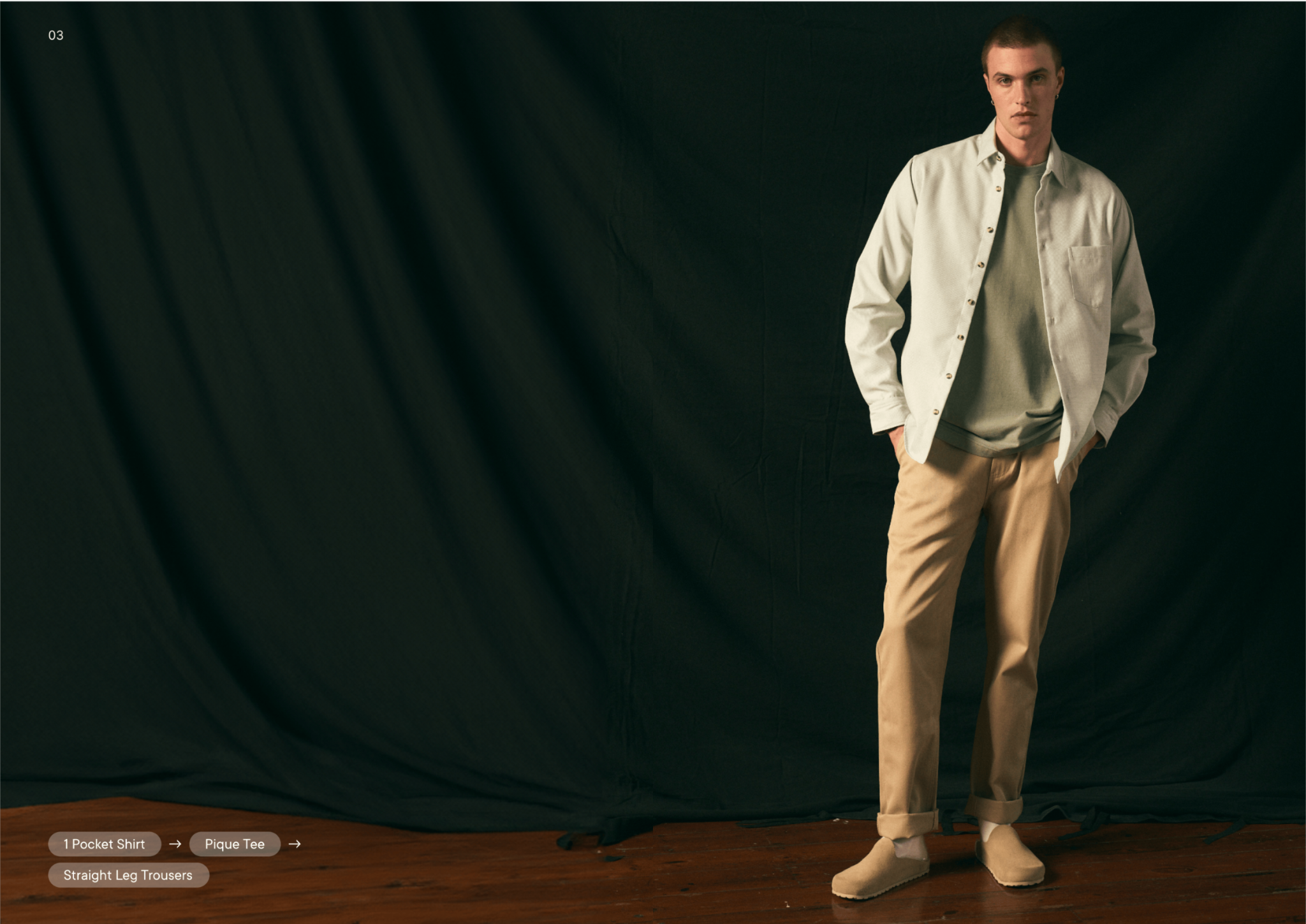 Man wearing a light-colored shirt and beige pants against a dark curtain background