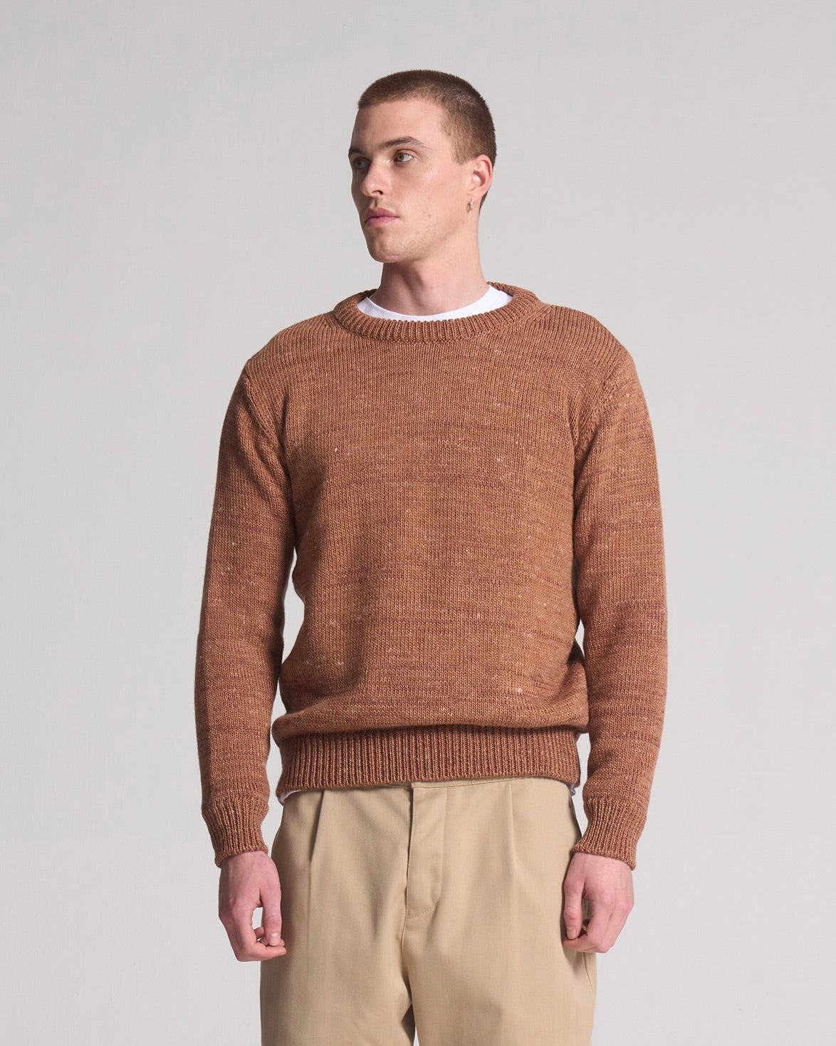 Man wearing a brown knitted sweater made from wool and linen and beige pants against a plain background
