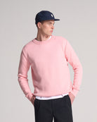 Person wearing a pink sweater made in wool and mohair, navy cap, and black pants on a grey background
