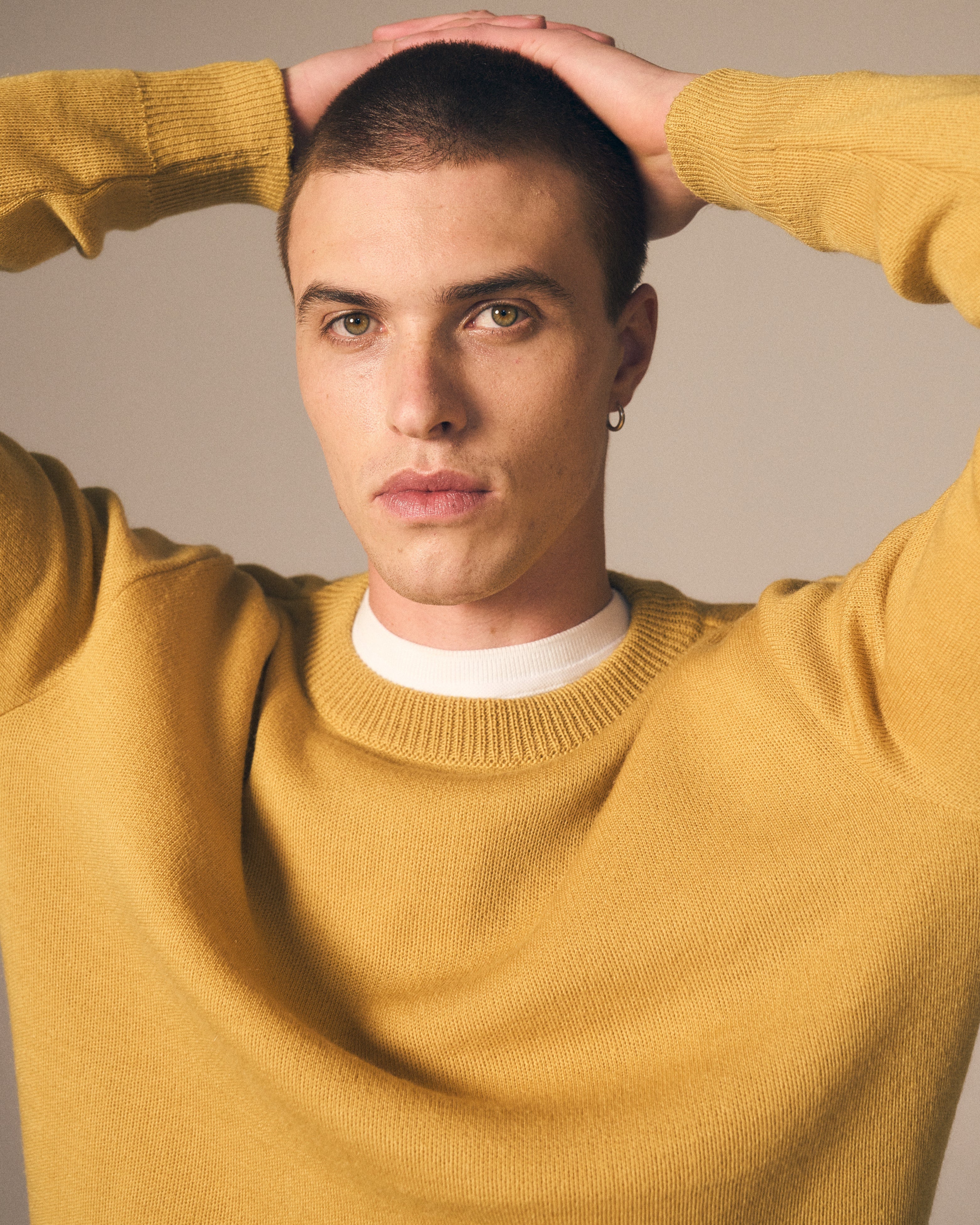 Man wearing a mustard yellow sweater with a plain background