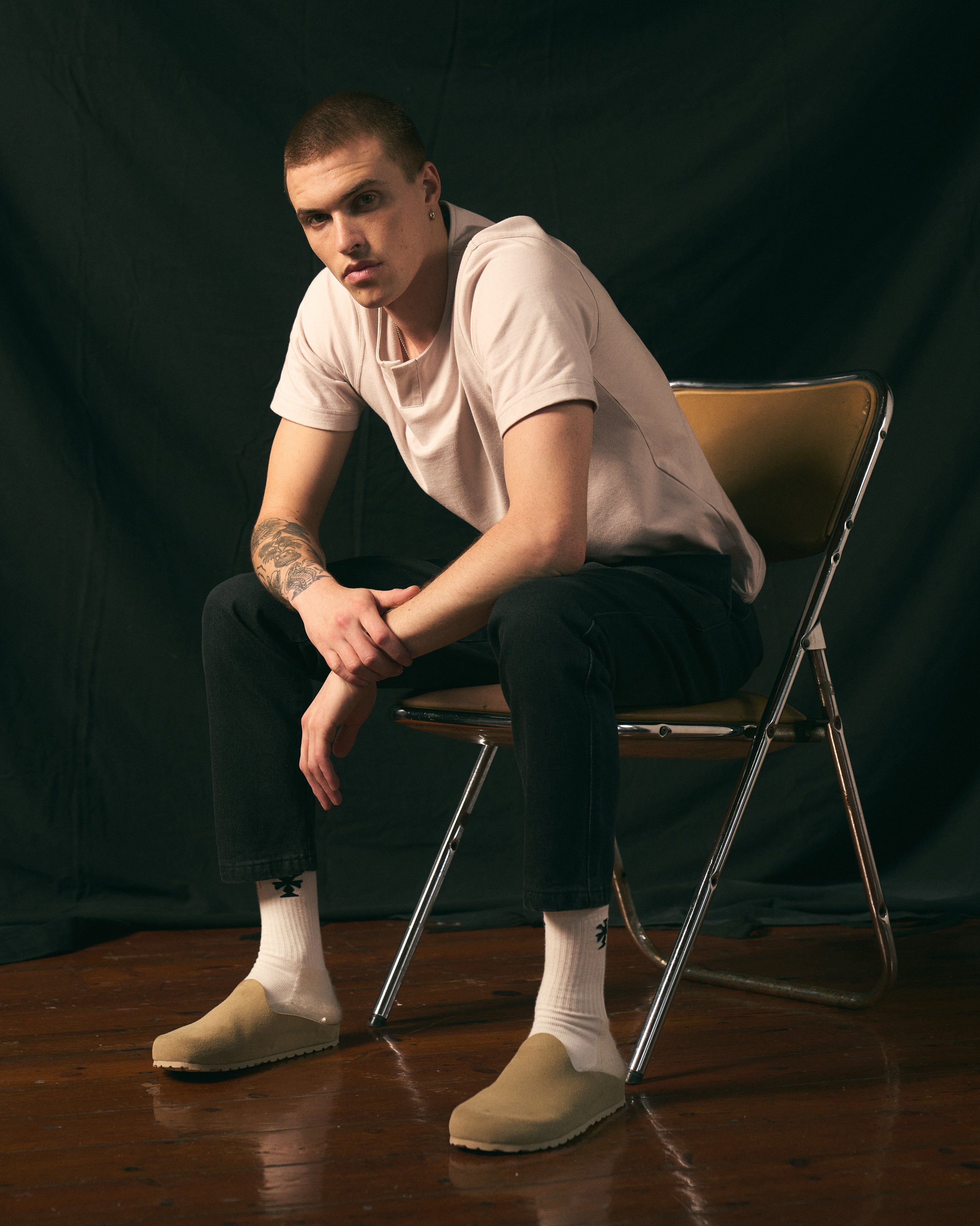 Man sitting on a chair against a black background wearing a henley t-shirt