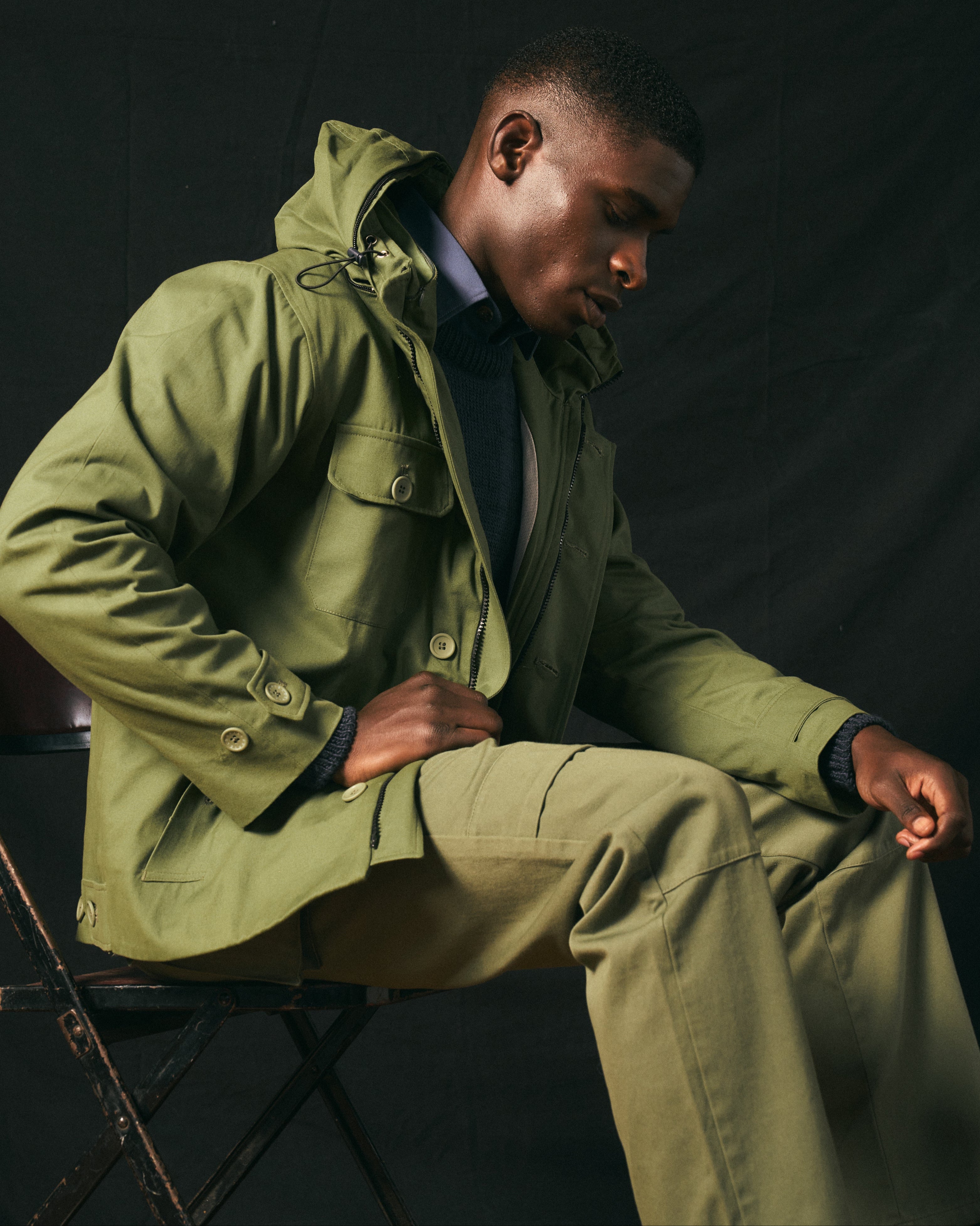 Man wearing a green coat sitting on a chair against a dark background