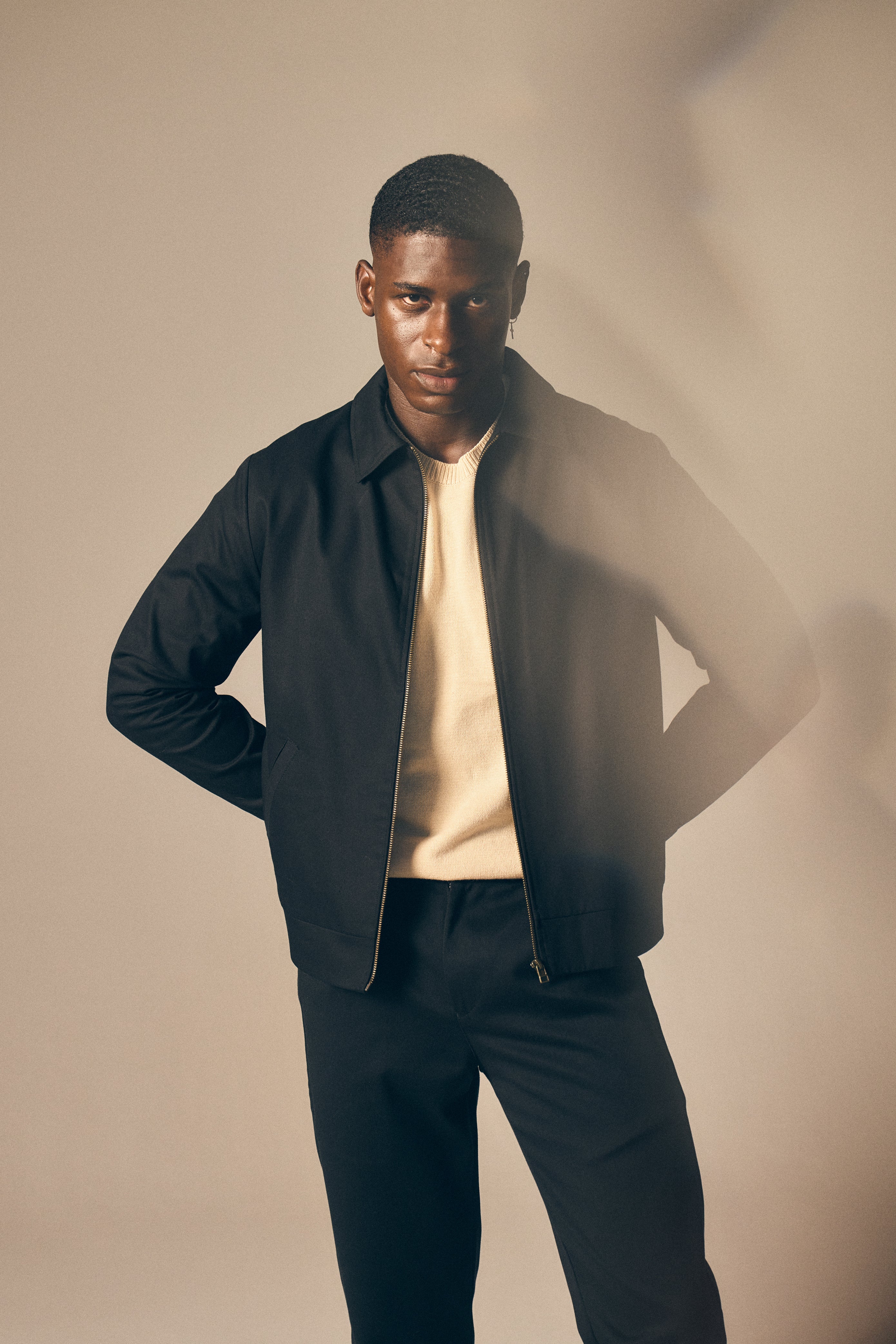 Man wearing a black jacket over a beige shirt with a plain background