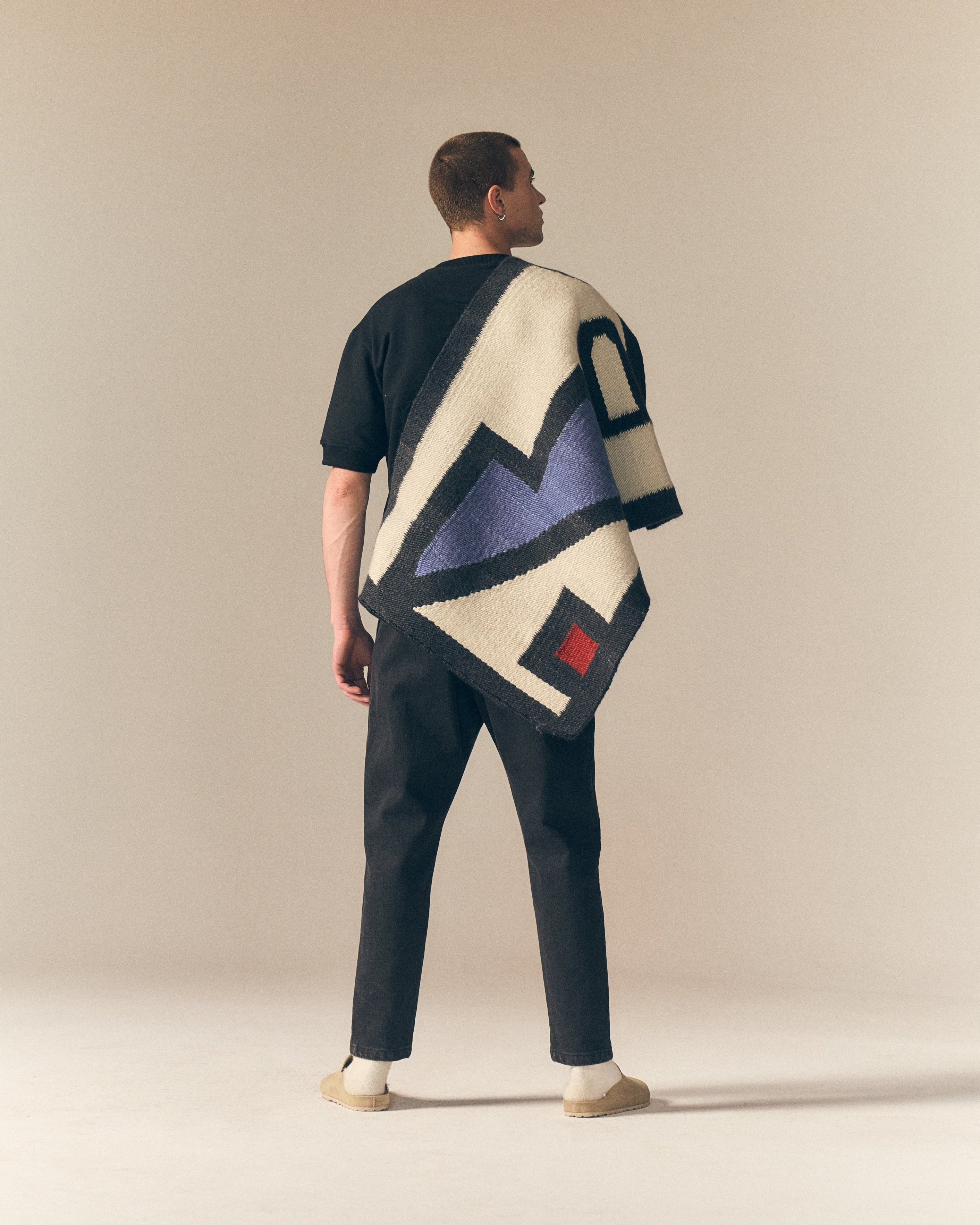 Man wearing a black short sleeve sweater with a plain background, holding the artwork as part of the Fields collaboration with the Ninevites.