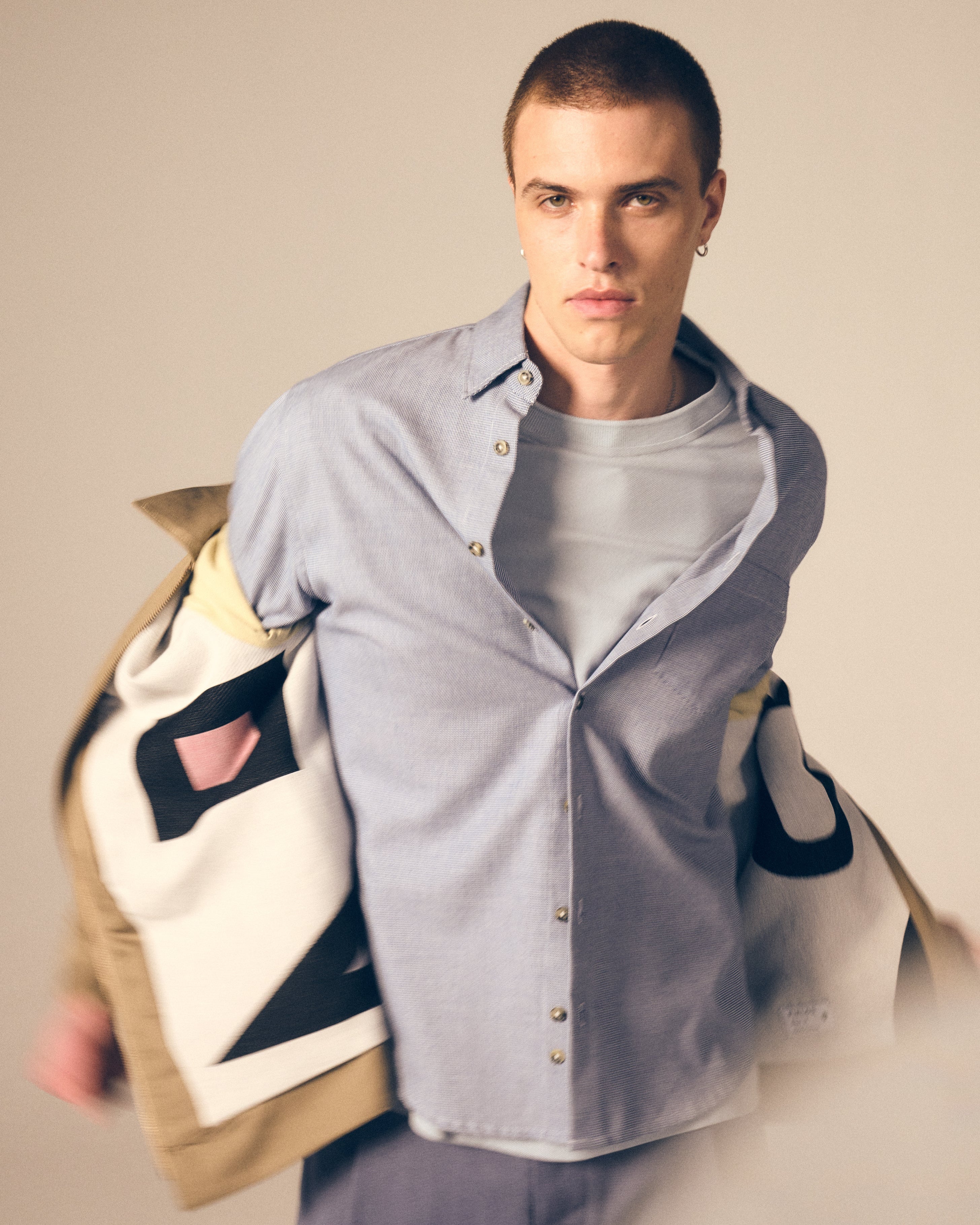 Man wearing a light grey t-shirt with a blue shirt and beige jacket over it