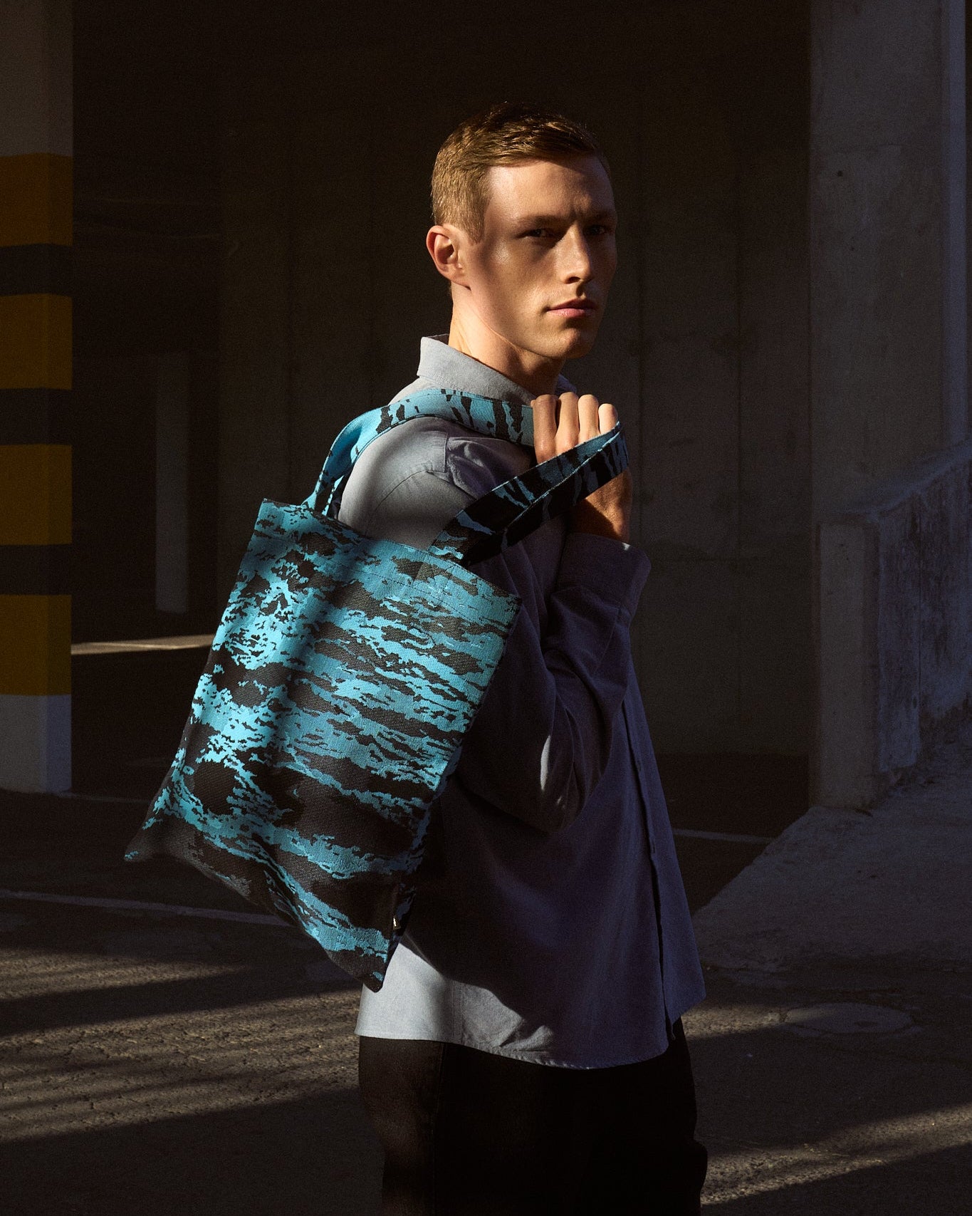 Man holding a blue camouflage bag in a dimly lit outdoor setting, featuring collaboration between Fields and Chris Soal