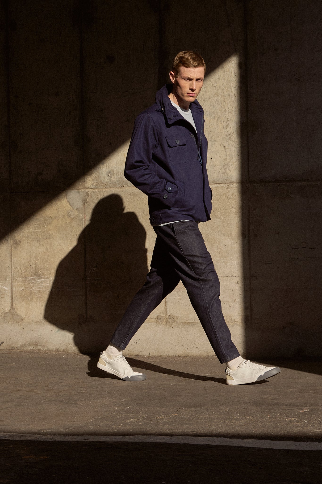 Man walking against a textured wall with a strong light and shadow effect