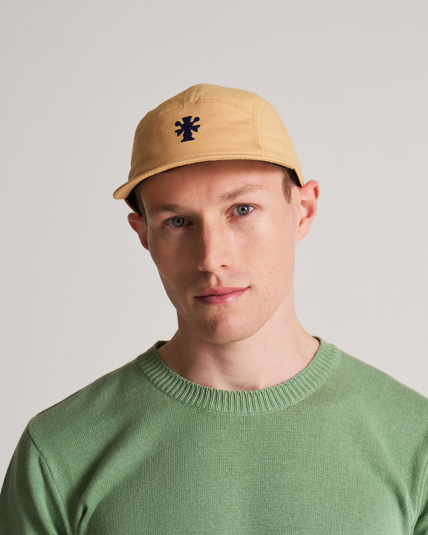 Man wearing 5 panel cap in the colour rattan with a green knitted t-shirt.