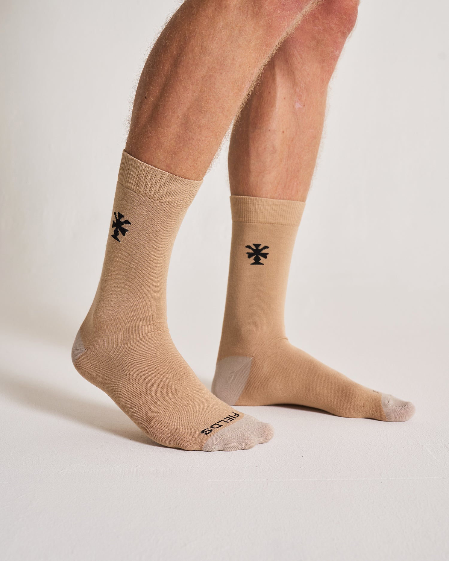 Beige socks with a black logo worn by a person on a light background