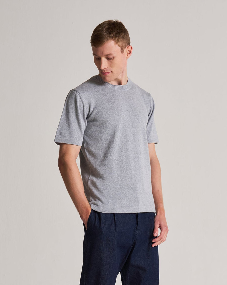 Man wearing a gray t-shirt and navy pants on a plain background