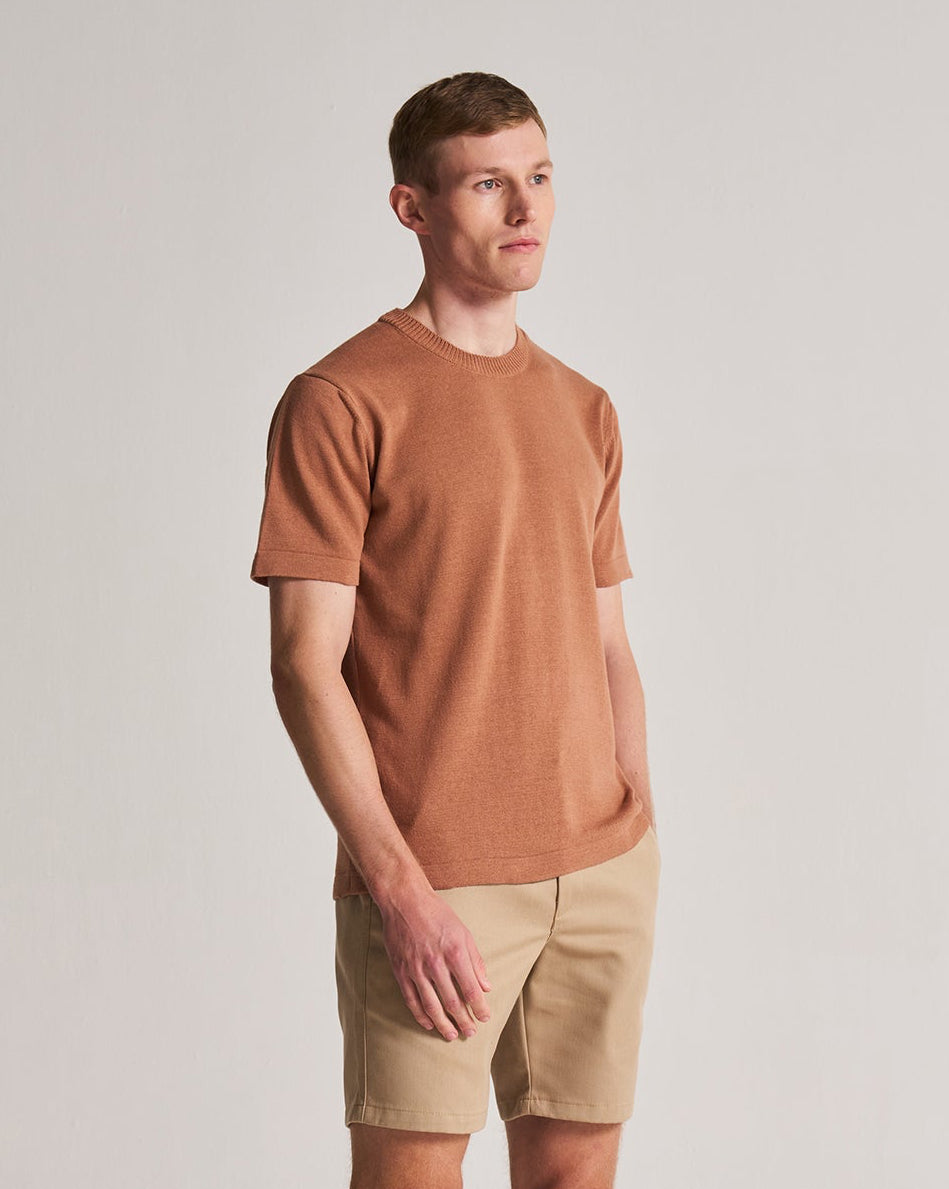 Man wearing a brown t-shirt and beige shorts on a plain background