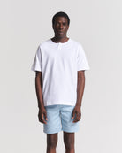 A man modeling a white short-sleeve t-shirt with a split crew neck and light blue shorts, standing against a light gray studio background.