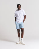 A man modeling a white short-sleeve henley t-shirt, light blue shorts, white crew socks, and white sneakers against a plain light gray studio background.