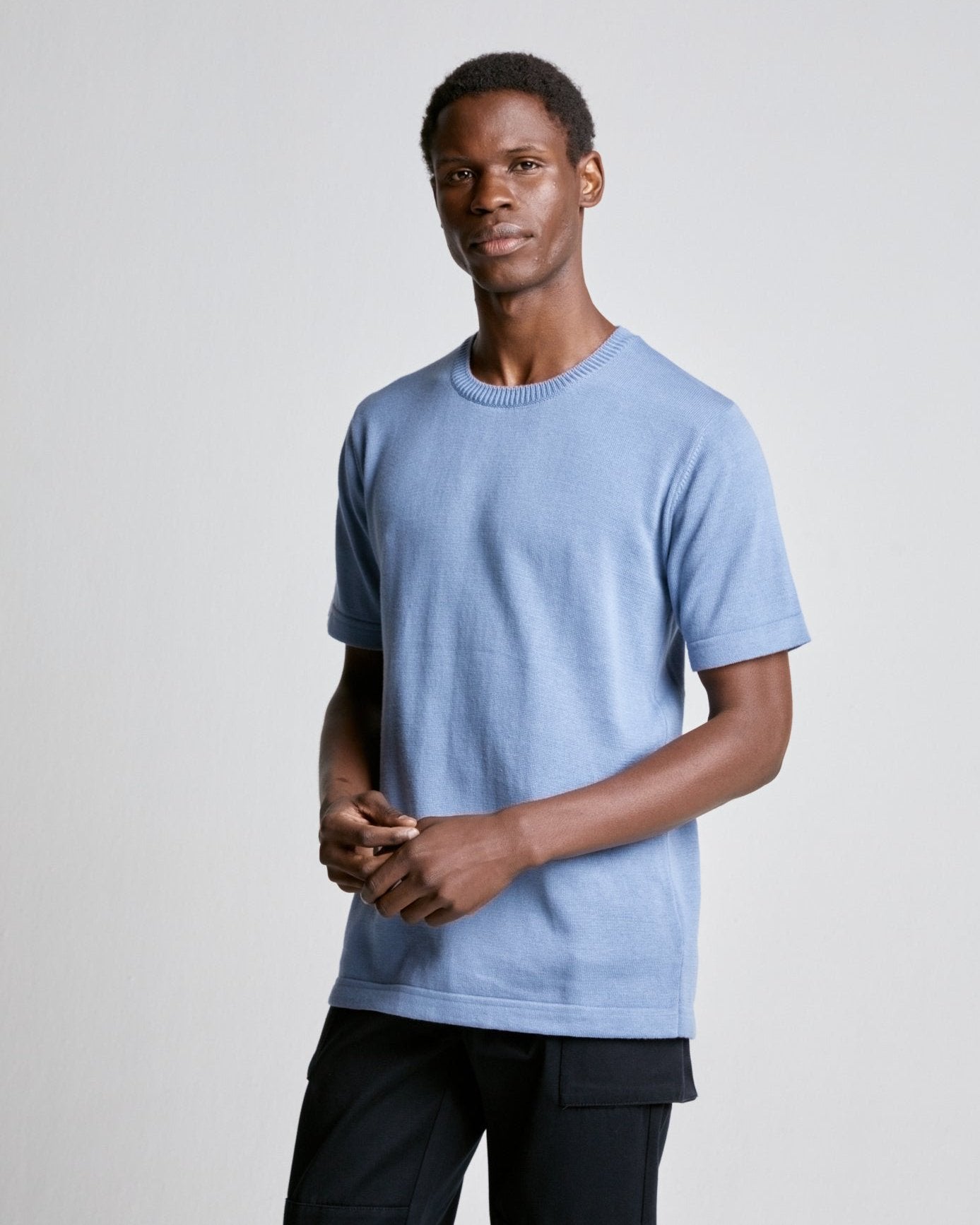 A person wearing a light blue, knitted, short-sleeved tee with a ribbed neck and mock back yoke detail.