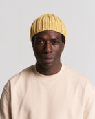 yellow knit beanie worn by a man in a beige top