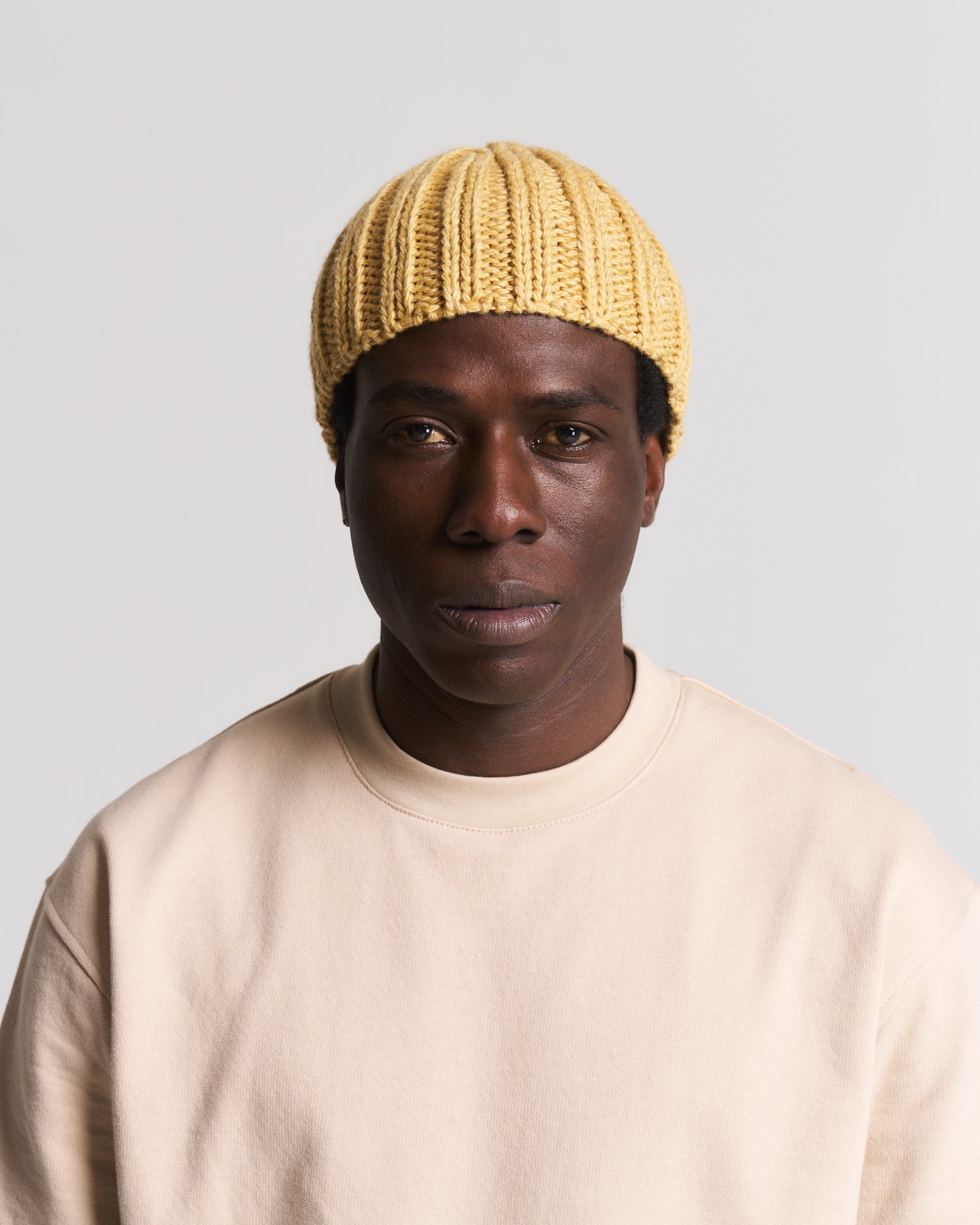 yellow knit beanie worn by a man in a beige top