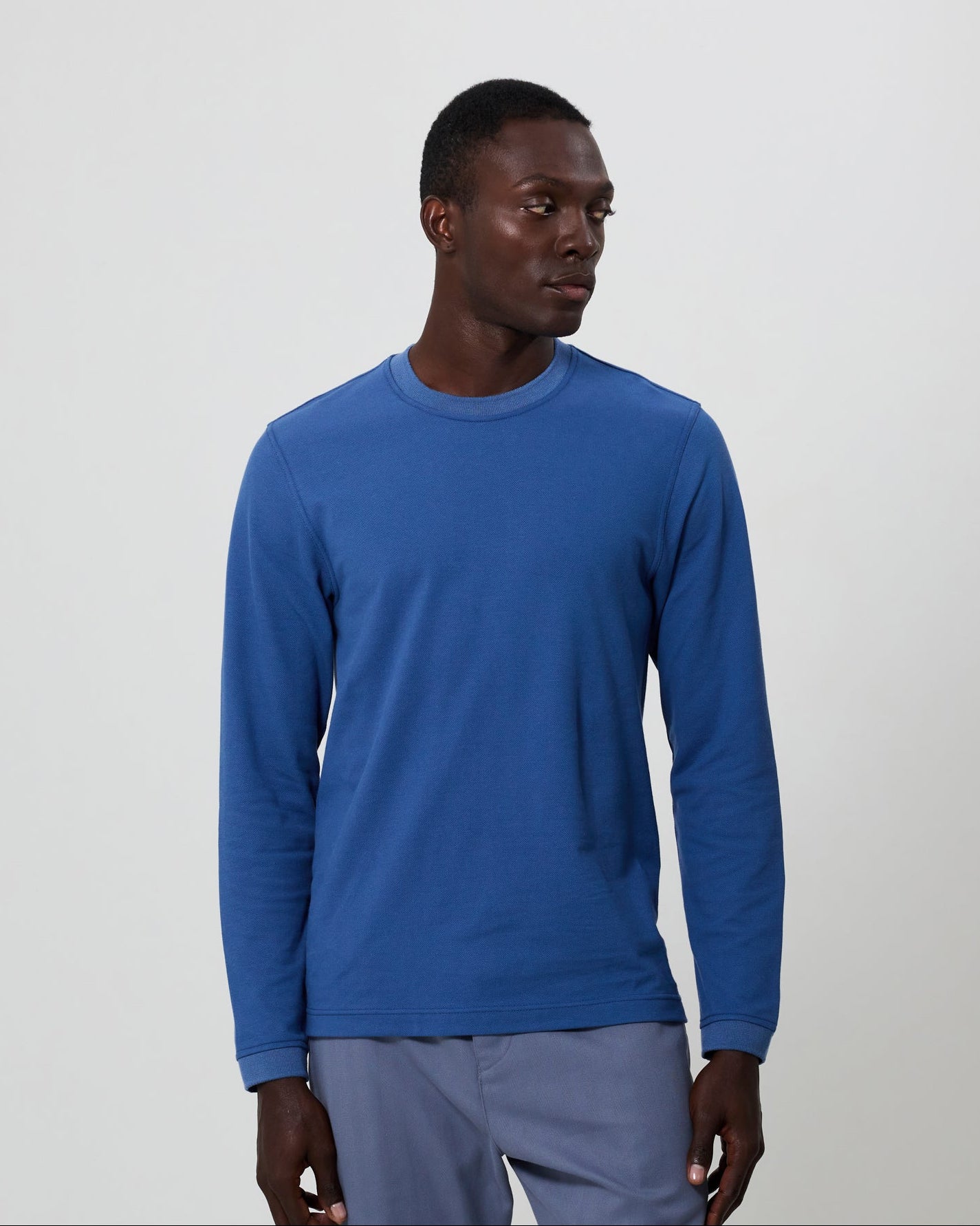 Man wearing a blue long-sleeve t-shirt with grey pants against a plain background. All from Fields. 